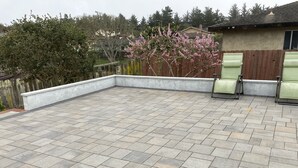 Eine Terrasse mit Steinplatten, einem Holzzaun und einem Baum mit rosa Blüten.
