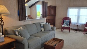 Uma sala de estar aconchegante com um sofá cinza, duas poltronas vermelhas, uma mesa de centro de madeira, um abajur e um espelho sobre o sofá.