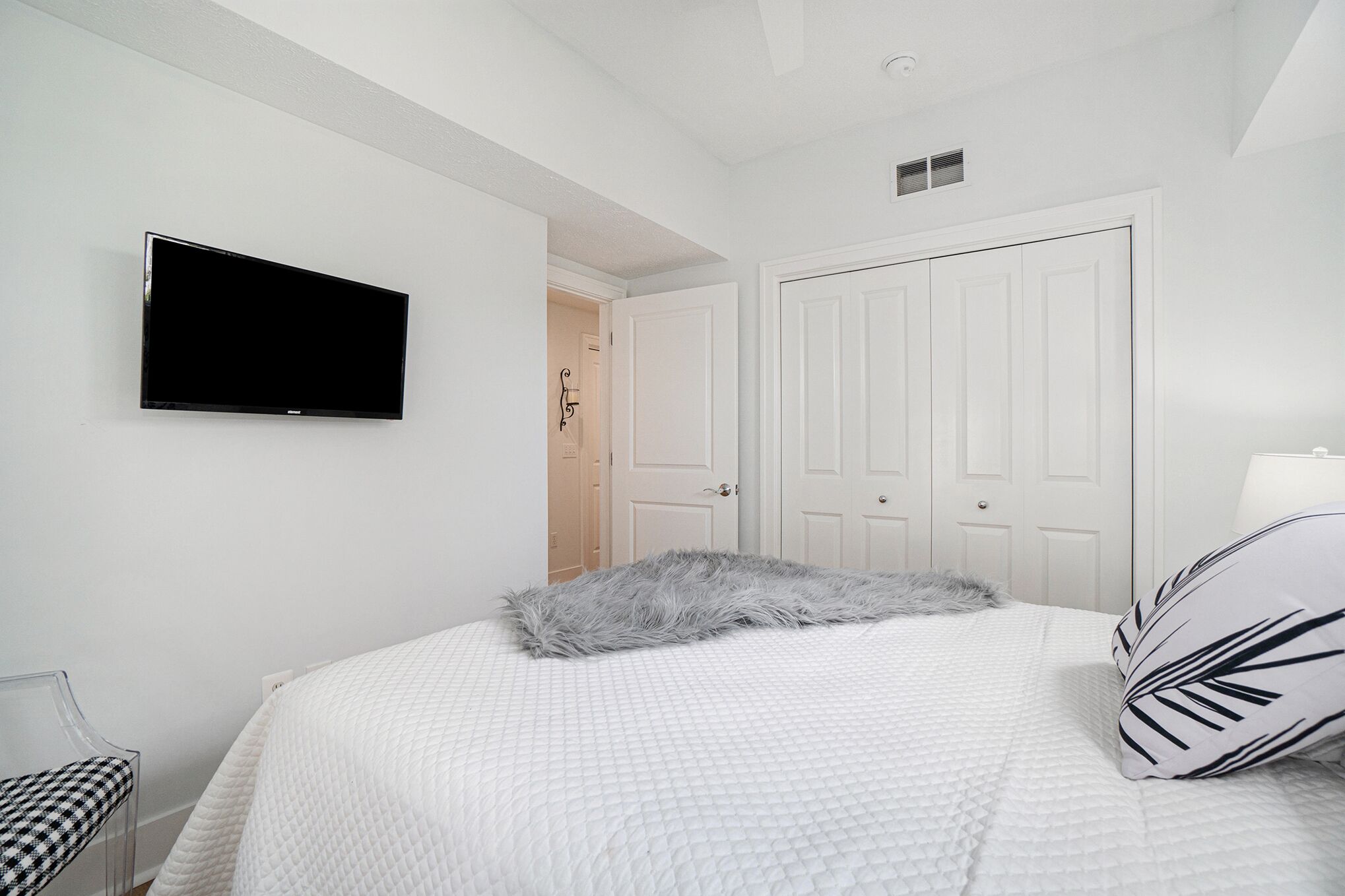 A bedroom with a bed, a television mounted on the wall, a door, and a chair.
