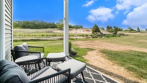 Une terrasse couverte, aménagée avec du mobilier d’extérieur, offrant une vue sur une pelouse et des arbres.