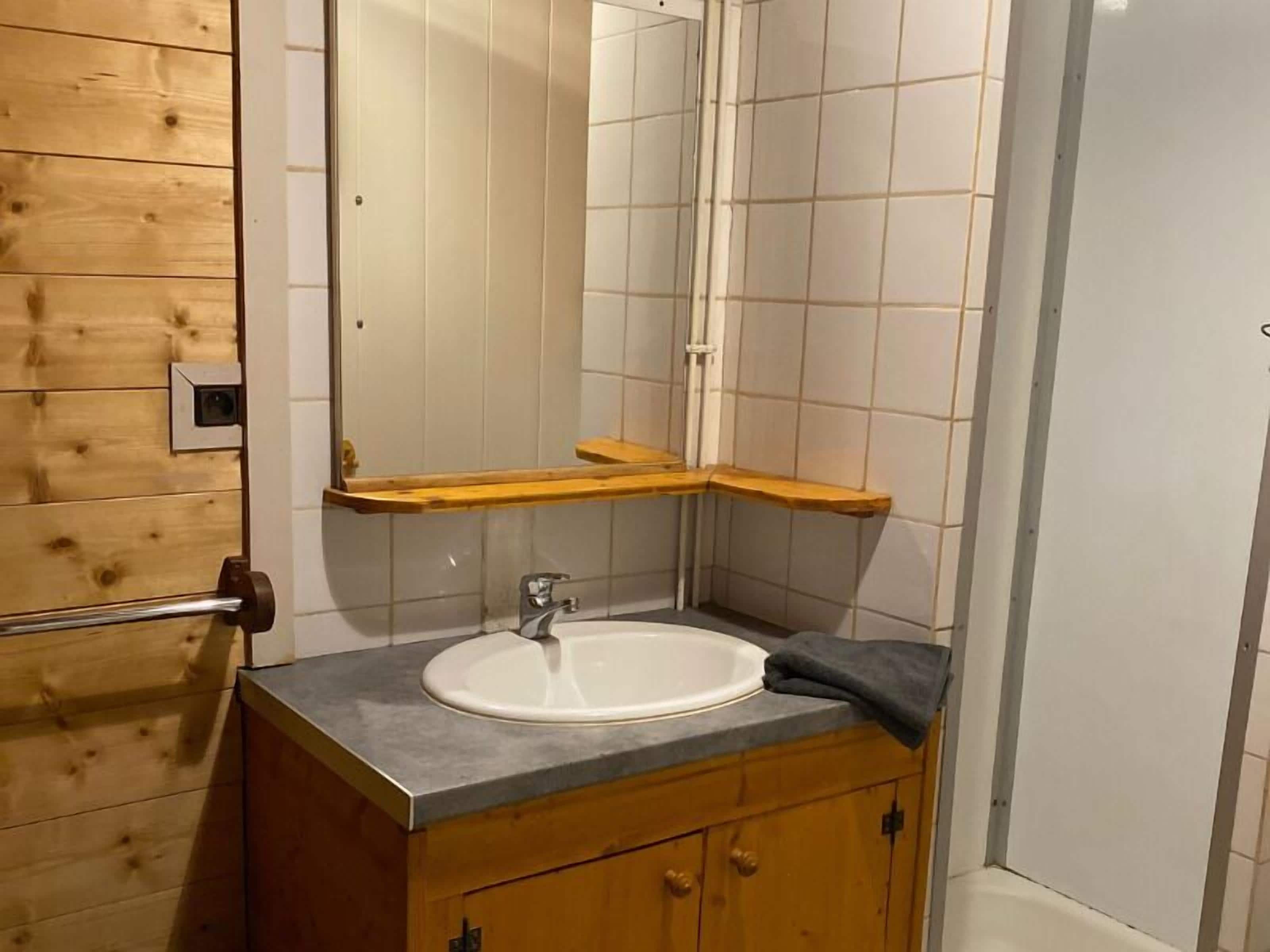 Een badkamer met een houten wastafelmeubel, een witte wasbak en een spiegel.