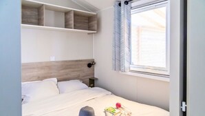A neatly made bed with a hat and a bag on it, a window with curtains, and built-in shelves above the bed. - Relais du Léman (Messery)