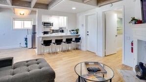 A modern living room with a sofa, a glass coffee table, and a kitchen area with white cabinets and a microwave. - Newport Beach Vacation Rental Near Beach & Pier (Newport Beach)