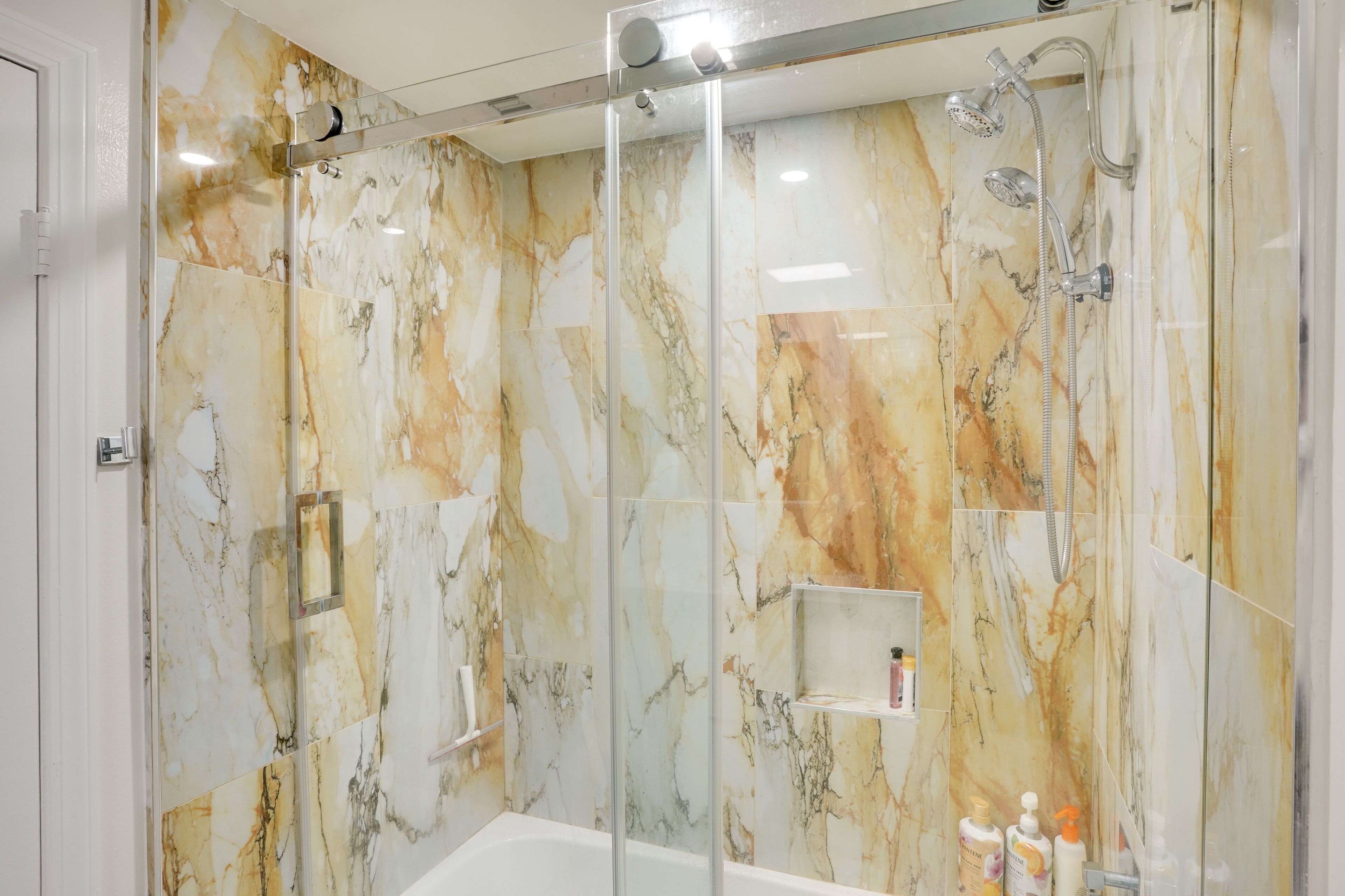 A modern bathroom with a glass-enclosed shower, marble walls, and a white bathtub.