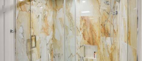 A modern bathroom with a glass-enclosed shower, marble walls, and a white bathtub.