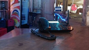 A rustic room with a wooden ceiling, a desk with a telephone and a computer, and a shelf with bottles. - Green Garden Guest House  (Arusha)