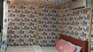 A small, cozy room with a patterned wallpaper, a single bed with a pink pillow, and a ceiling fan. - Green Garden Guest House  (Arusha)