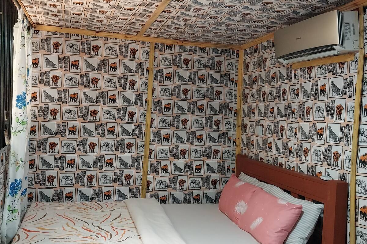 A small, cozy room with a patterned wallpaper, a single bed with a pink pillow, and a ceiling fan.