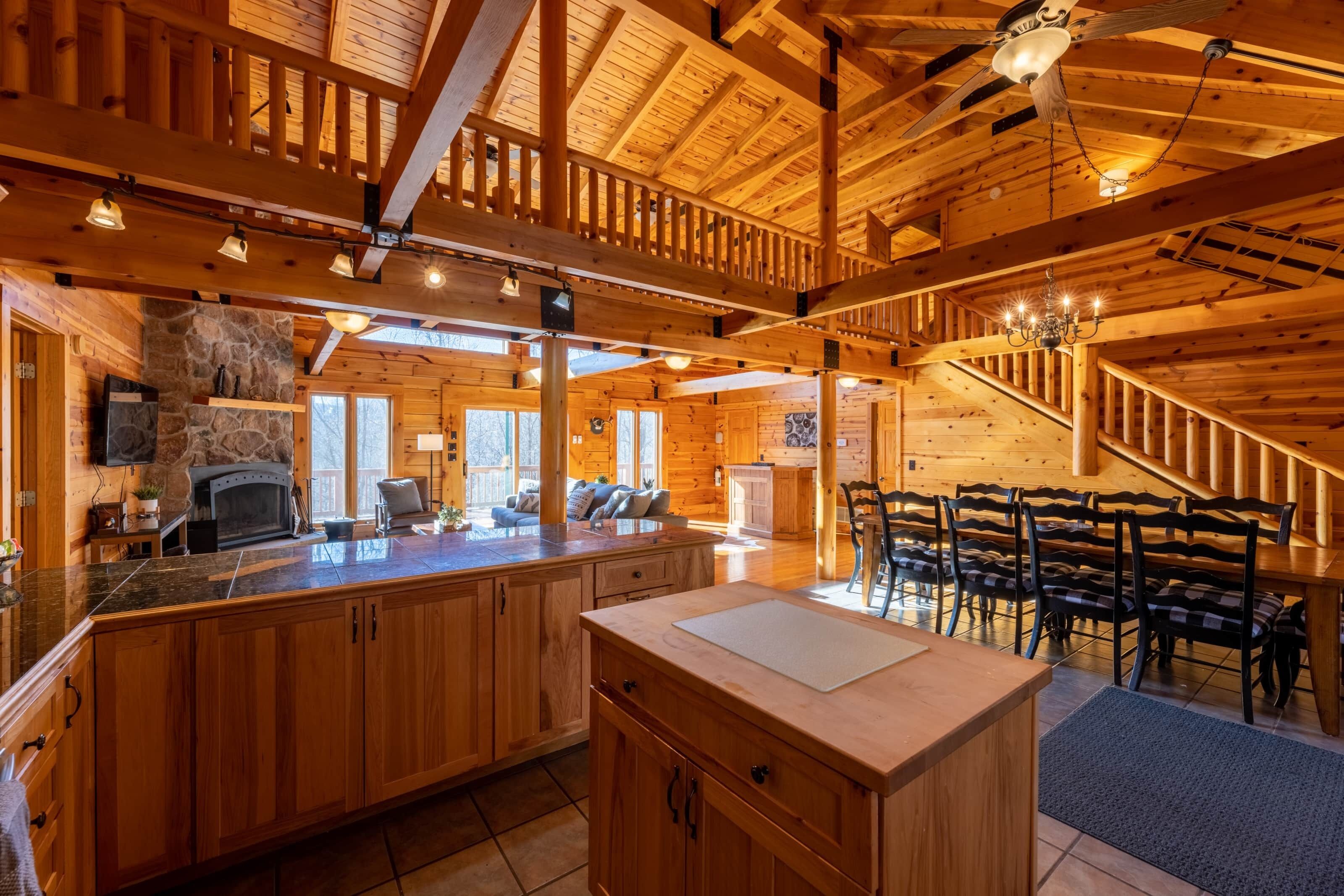 Une vaste cabane en bois dotée d’une grande cuisine, d’un coin repas et d’une cheminée en pierre.