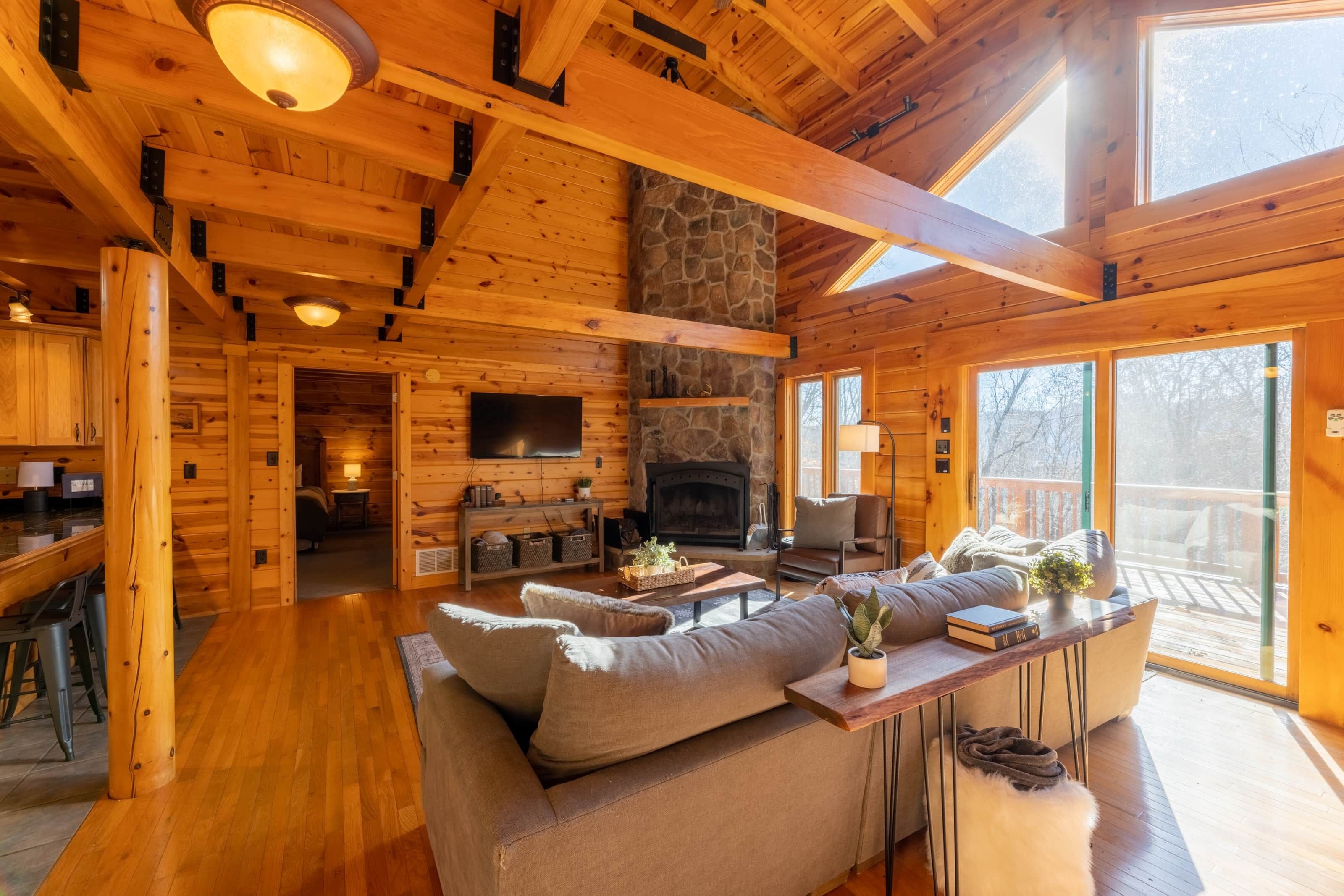 Un intérieur de chalet chaleureux avec une cheminée en pierre, des poutres en bois, un canapé et un coin repas.