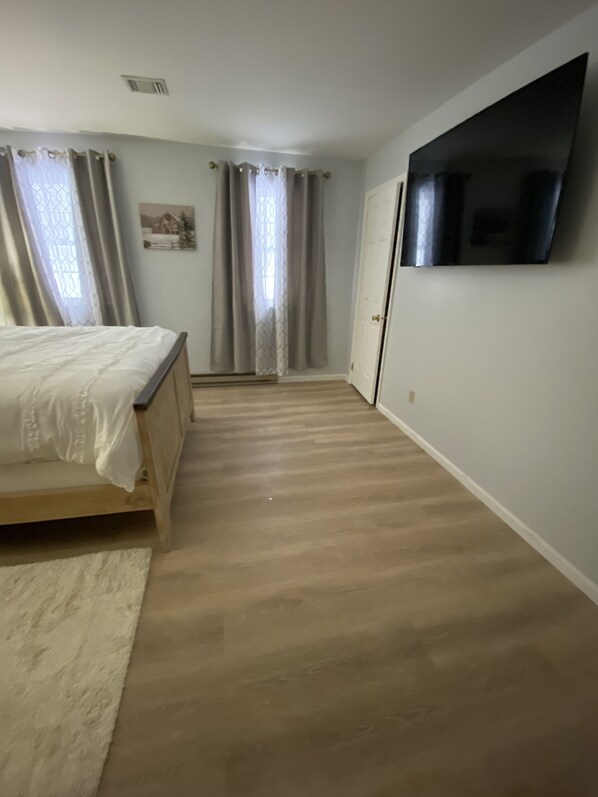 Ein Schlafzimmer mit Bett, einem an der Wand montierten Fernseher, Holzboden und einer Tür.