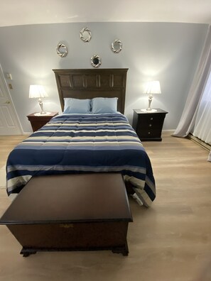 Ein Schlafzimmer mit einem Bett, zwei Nachttischen mit Lampen, einer Holzbank und dekorativer Wandgestaltung.