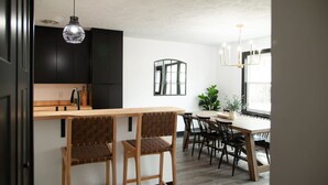 A modern kitchen with dark cabinets, a wooden island, and a dining area with a table and chairs.