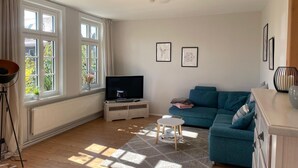 Un salón amplio con un gran ventanal, un televisor, un sofá azul y una mesita.
