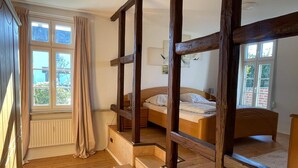 Un dormitorio con escalera de madera, cama, ventana con cortinas y radiador.