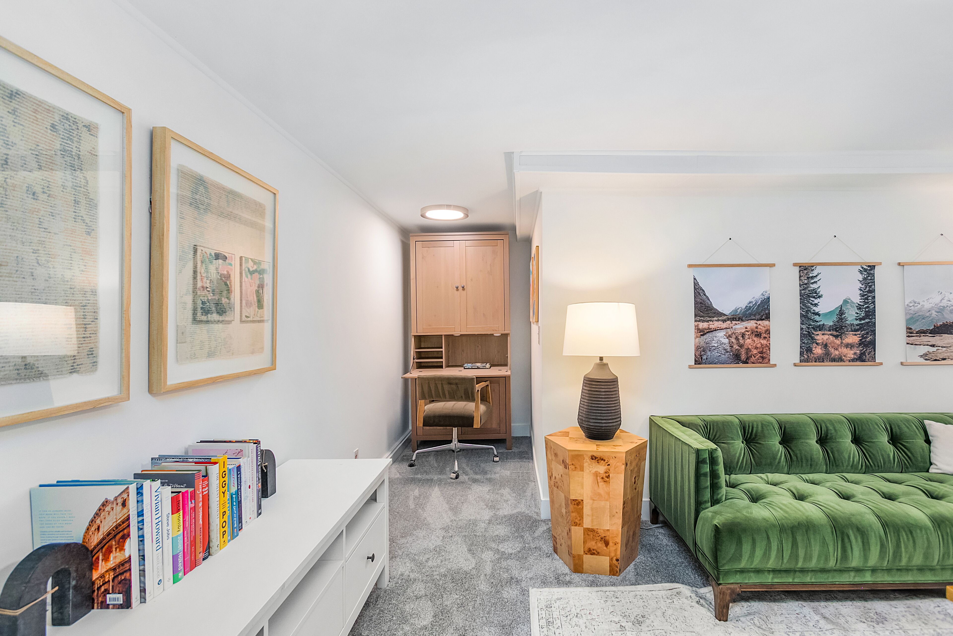 A modern living room with a green sofa, a white desk, and a bookshelf filled with books.
