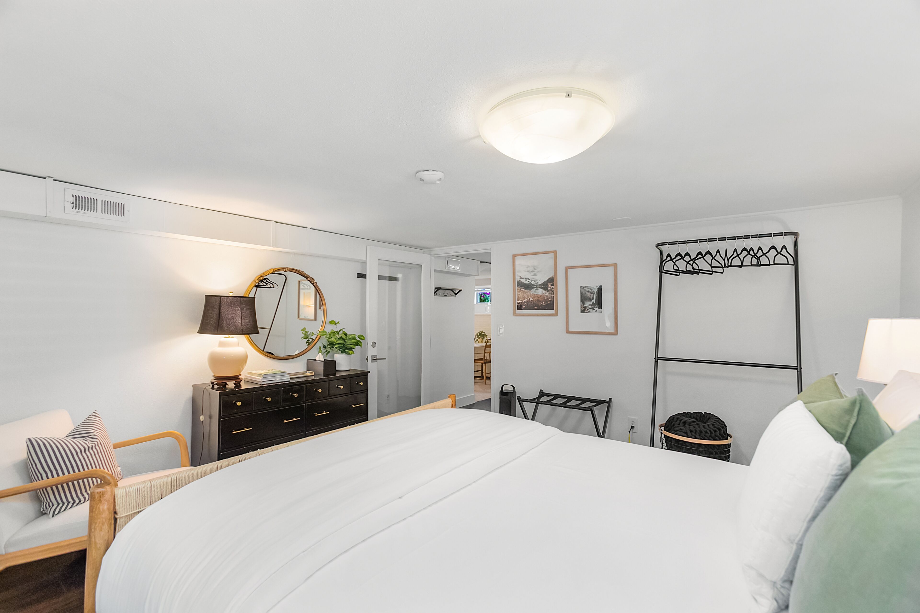 A modern bedroom with a large bed, a dresser, a mirror, and a wall-mounted rack.