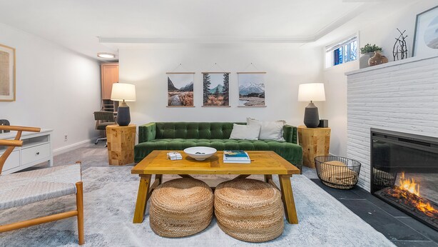 A modern living room with a green sofa, wooden coffee table, and a fireplace. There are three framed pictures on the wall, a lamp on each side of the sofa, and a small table with a bowl and book. - Lilac in Law (Seattle)
