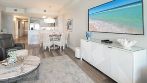 A modern living room with a marble coffee table, a white cabinet with decorative items, and a large beach-themed painting on the wall. - LAST Minute Cancellation! Luxurious gorgeous condo and includes beach service! (Panama City Beach)