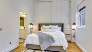 A modern bedroom with a large bed, a wooden floor, and a white brick wall.