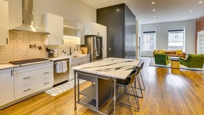A modern kitchen with a central island, stainless steel appliances, and a dining area with green chairs.