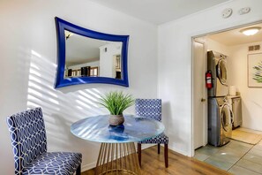 A room with a round glass table, two patterned chairs, a potted plant, and a blue-framed mirror.