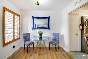 A dining area with a round glass table, two patterned chairs, a blue-framed mirror, and a potted plant.