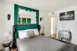 A neatly arranged bedroom with a large bed, a green accent wall, a side table, and a dresser.