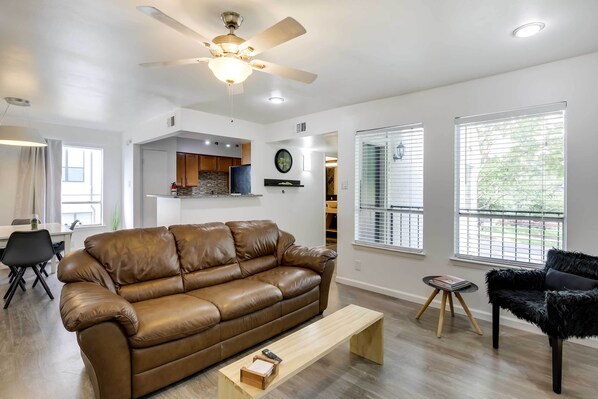 A modern living room with a brown leather sofa, a black furry chair, a wooden coffee table, and a ceiling fan.