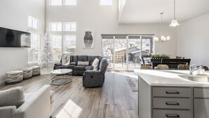 Een ruime zithoek met een grote grijze modulaire bank, een ronde salontafel en een witte kerstboom.