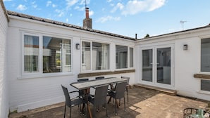 A patio with a table and chairs, a chimney, and a white building with large windows and a sliding door. - A stunning location for exploring the stunning North Norfolk Coast. (Brancaster Staithe, near King&rsquo;s Lynn)