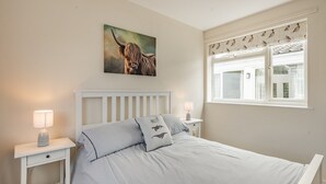 A bedroom with a bed, two bedside tables, a window with curtains, a wall-mounted picture, and a lamp on each table. - A stunning location for exploring the stunning North Norfolk Coast. (Brancaster Staithe, near King&rsquo;s Lynn)