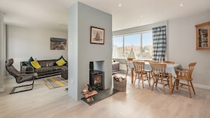 A modern living room with a fireplace, a dining area with wooden chairs, and a sofa with cushions. - A stunning location for exploring the stunning North Norfolk Coast. (Brancaster Staithe, near King&rsquo;s Lynn)