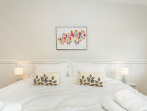 Een opgemaakt bed met twee kussens, een abstract kunstwerk aan de muur, en twee nachtlampjes.