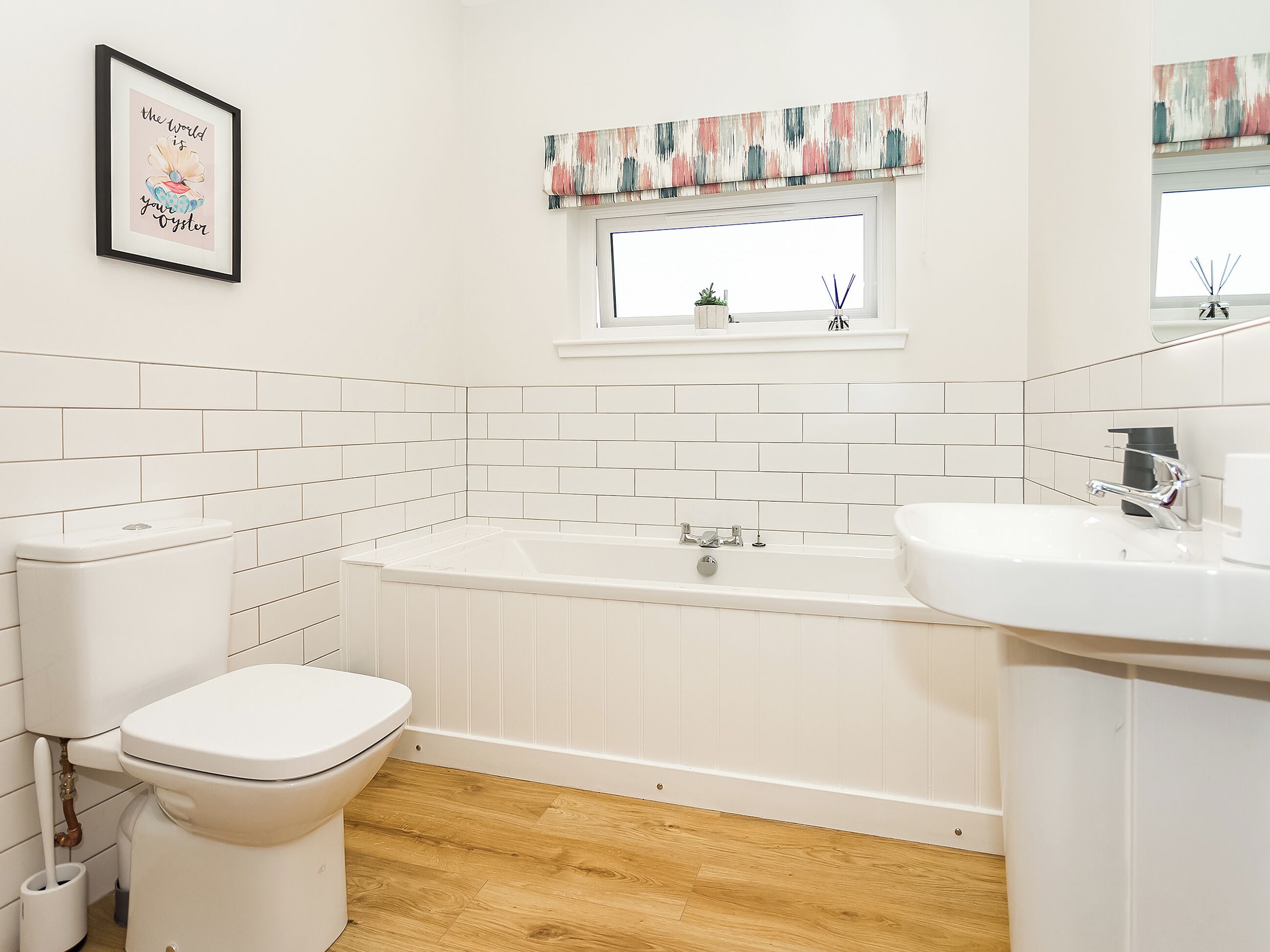 Une salle de bain avec des toilettes, une baignoire et un lavabo, des carreaux blancs, un plancher en bois et une citation encadrée au mur.