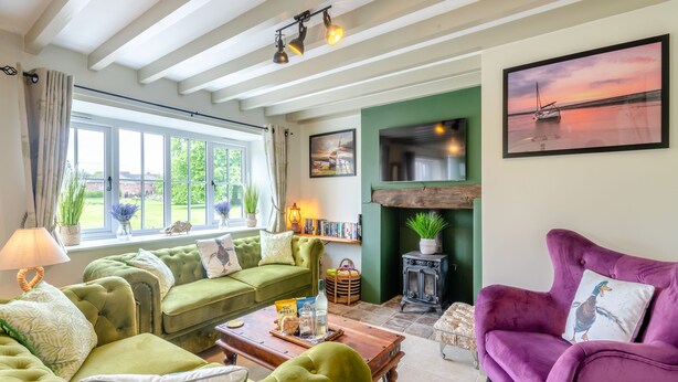 A cozy living room with a green sofa, a purple armchair, a fireplace, and a large window with curtains. - 3 bedroom accommodation in South Creake, near Fakenham (South Creake, near Fakenham)
