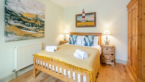 A bedroom with a wooden bed, two nightstands with lamps, a painting of a lighthouse, a large abstract painting, and a wooden wardrobe. - 3 bedroom accommodation in South Creake, near Fakenham (South Creake, near Fakenham)