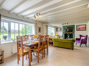 Un coin repas avec des chaises en bois et une table dressée pour six personnes, un canapé vert, un fauteuil violet et une cheminée.