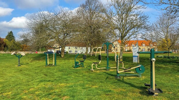 Un parc équipé d’installations d’exercice, avec des arbres et un bâtiment en arrière-plan.