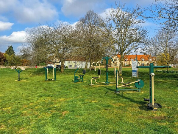 Un parque con equipo de ejercicio, árboles y un edificio al fondo.