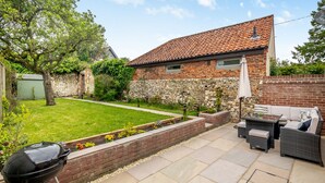 A backyard with a barbecue grill, outdoor furniture, and a stone wall. - 3 bedroom accommodation in South Creake, near Fakenham (South Creake, near Fakenham)