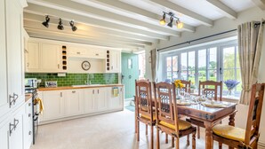 A spacious kitchen with white cabinets, a green backsplash, and a dining area with wooden chairs and a table set for four. - 3 bedroom accommodation in South Creake, near Fakenham (South Creake, near Fakenham)