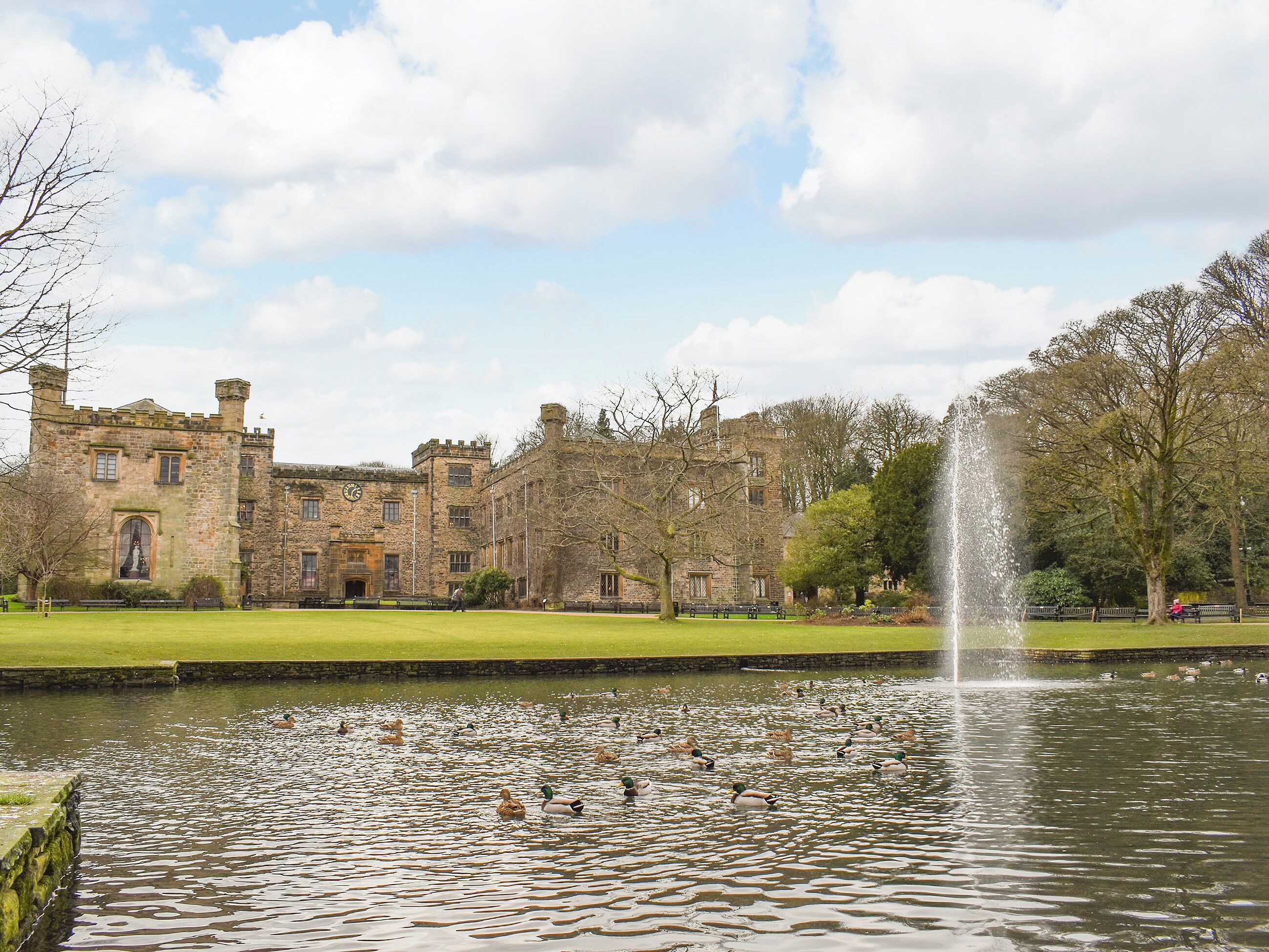 A historic stone building with a large lawn and a fountain in the foreground.