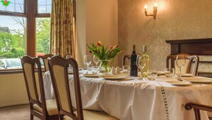 A dining room with a table set for four, chairs, a vase with flowers, wine bottles, and a wall-mounted light fixture. - 4 bedroom accommodation in Clitheroe (Clitheroe)
