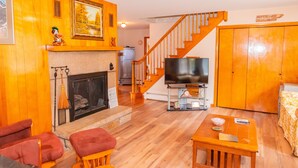 A living room with a fireplace, wooden furniture, a TV on a stand, and a staircase leading to another room. - The Big House in the Heart of Errol (Errol)