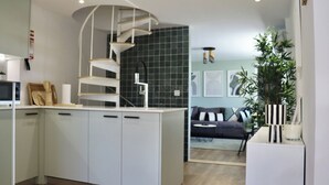 A modern kitchen with a central island, a spiral staircase, a dining area with a sofa, and a potted plant. - Lisbon, T2 renewed duplex with river view, Beato (Lisboa ciudad)