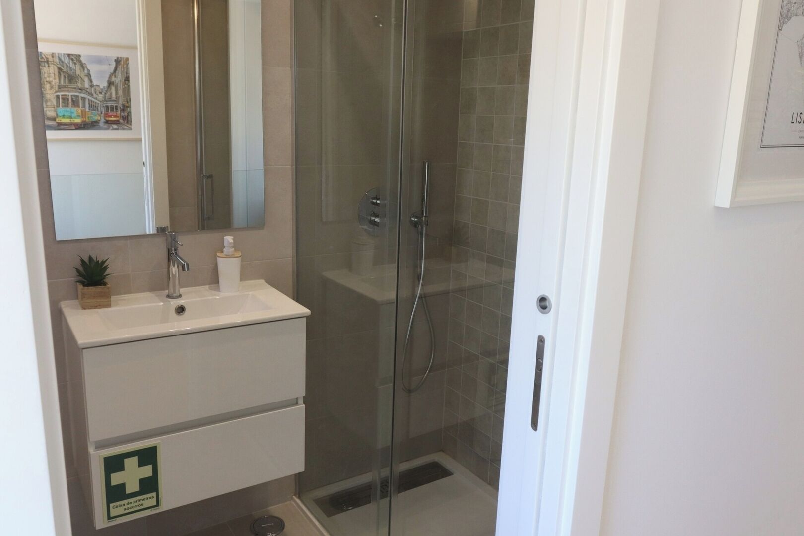 A bathroom with a glass-enclosed shower, a sink with a mirror, and a first aid kit sign.