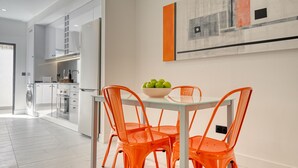 A modern kitchen with white cabinetry, a glass-top table, and orange chairs.