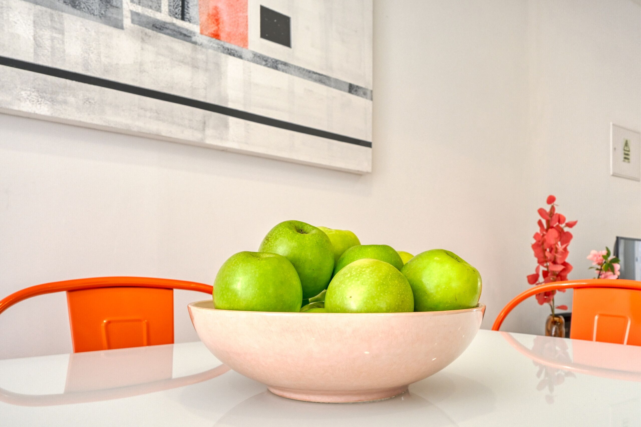 Un saladier de pommes vertes sur une table blanche, avec des chaises orange.