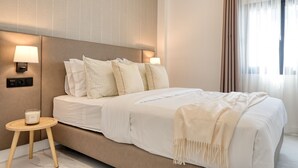 A modern hotel room with a large bed, two bedside lamps, a small round table with a candle, and a large window with curtains.